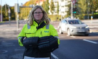 Kvinne i gul jakke holder opp store biter av bildekk. Vei i bakgrunnen. 